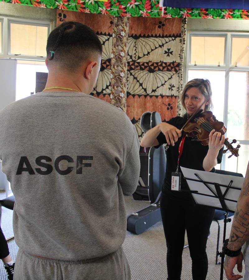 A violinist plays her instrument, facing a man who is wearing a gret tee-shirt and the words ASCF printed on the back